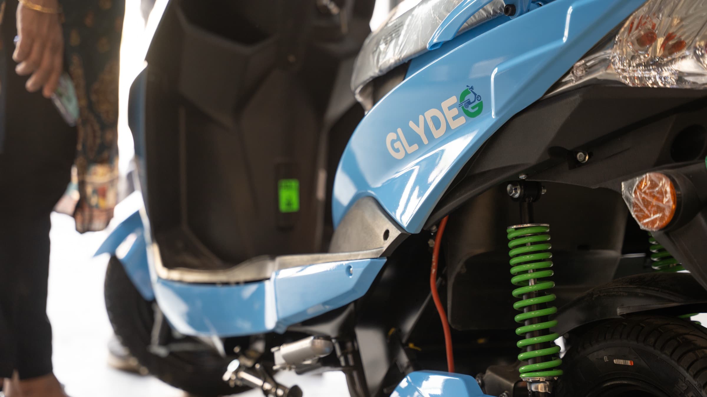 Close-up of a Glyde scooter’s side panel, showing the GLYDE badge and green rear spring.