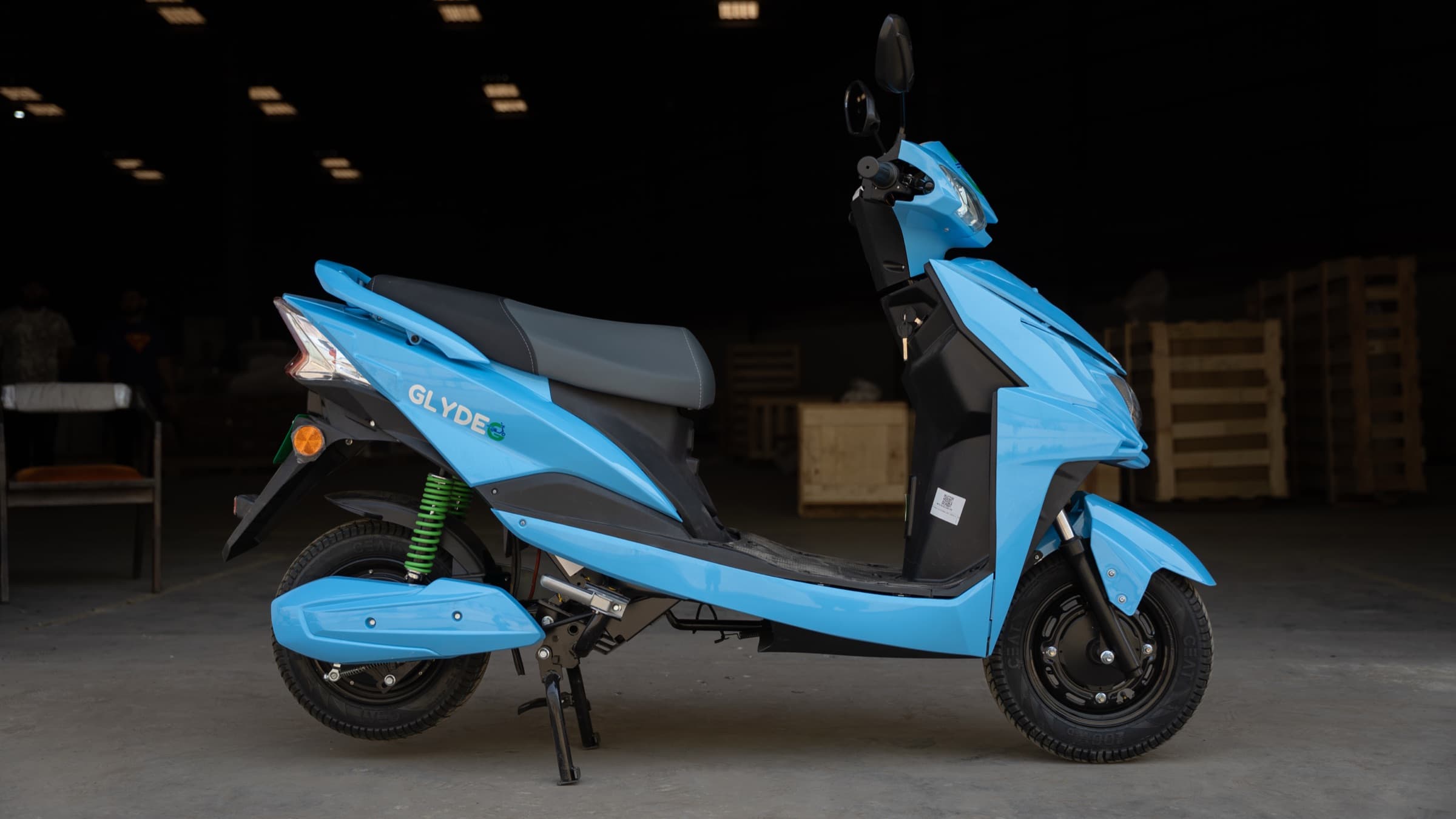 A Glyde electric scooter in profile, light blue with the GLYDE badge and green suspension.